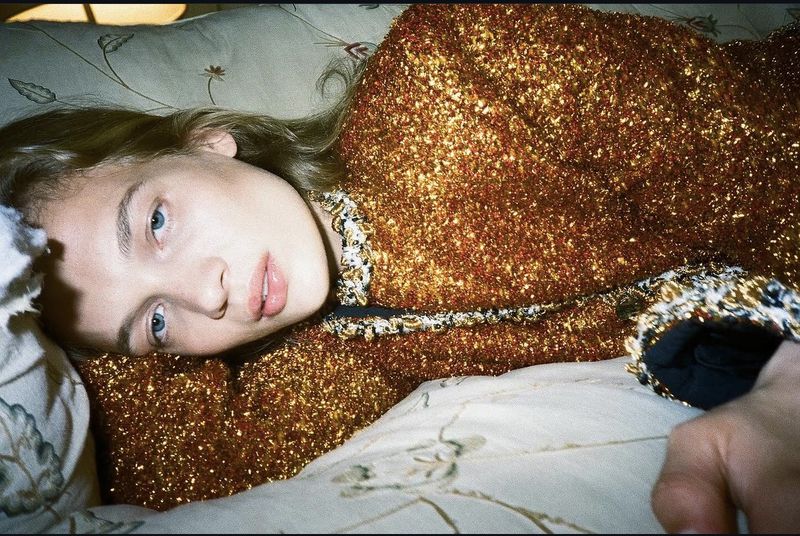 Model lying on a patterned bed wearing a metallic gold textured jacket for Self Service magazine project Virtualy