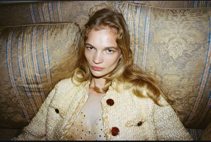 Model Caitlin Soetendal wearing a textured tweed jacket seated against a patterned vintage sofa in a portrait by Tess Petronio.