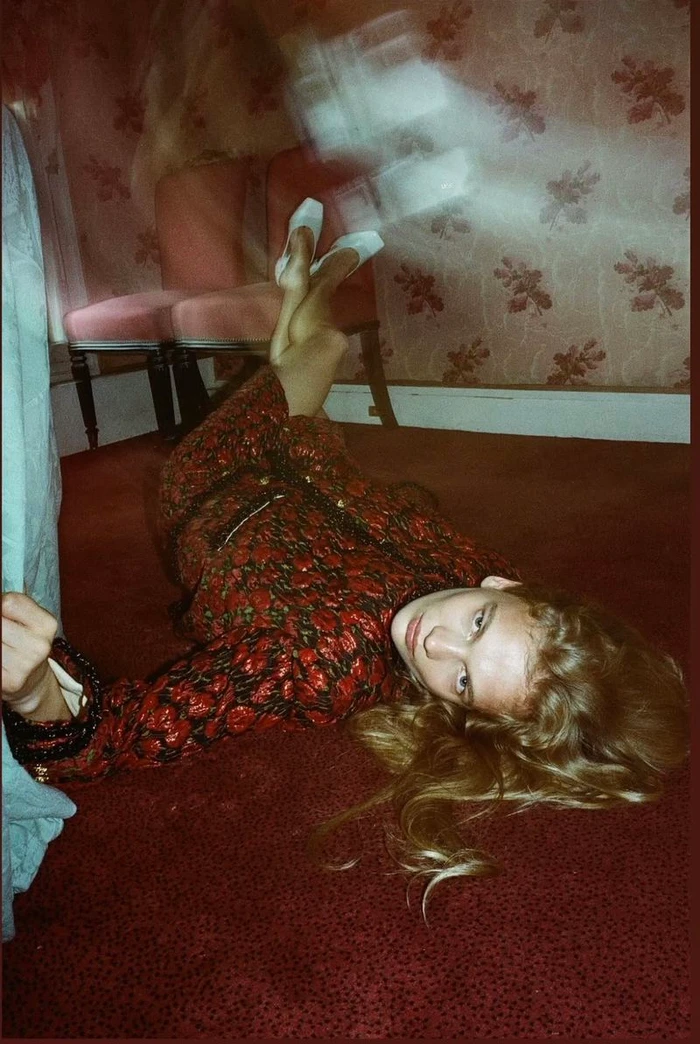 Model lying on red patterned carpet in a red patterned room with motion blur on feet