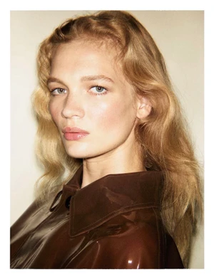 Close-up portrait of a blonde model wearing a glossy brown jacket against a neutral backdrop