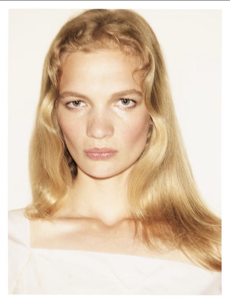 Portrait of a blonde woman with wavy hair and natural makeup against a plain white background
