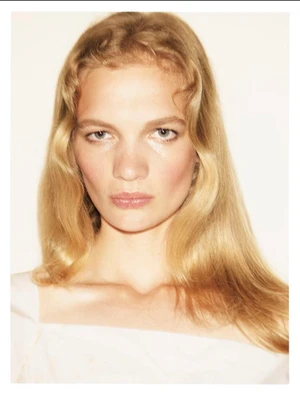 Portrait of a blonde woman with wavy hair and natural makeup against a plain white background