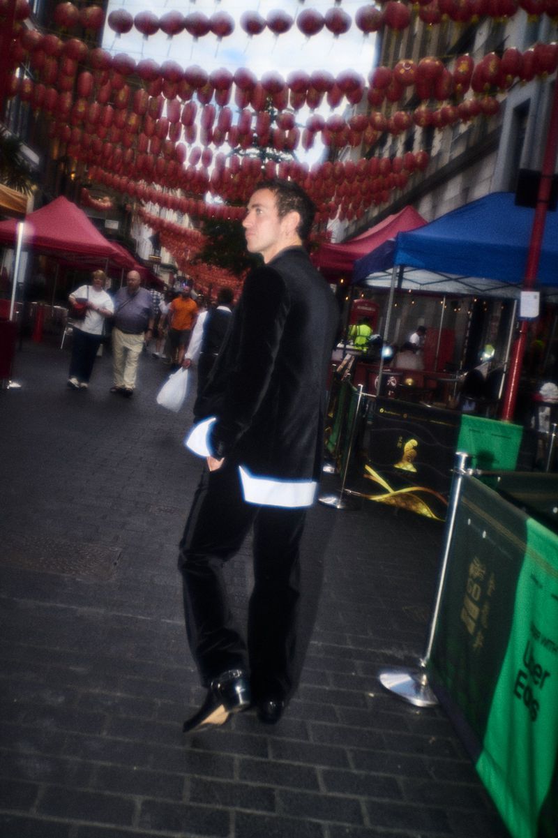 Man wearing a black velvet suit with white cuffs walking down a street under red lanterns for Numero Netherlands