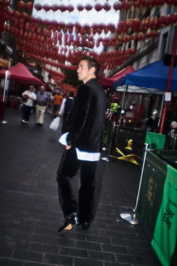 Man wearing a black velvet suit with white cuffs walking down a street under red lanterns for Numero Netherlands