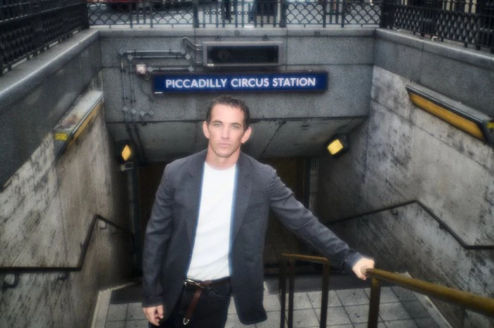 Man standing on the stairs outside Piccadilly Circus station wearing a dark blazer over a white t-shirt