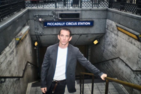 Man standing on the stairs outside Piccadilly Circus station wearing a dark blazer over a white t-shirt