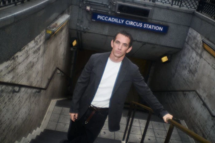 Man standing on the stairs of Piccadilly Circus Station wearing a dark blazer over a white t-shirt for Numero Netherlands.