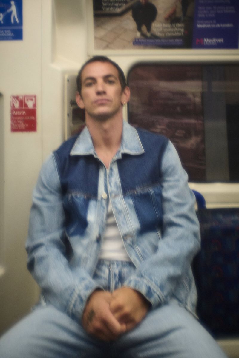 Alex Fine seated on public transport wearing a denim jacket and white t-shirt for Numero Netherlands