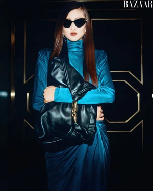 Model in blue turtleneck dress holding a large black leather handbag wearing dark sunglasses