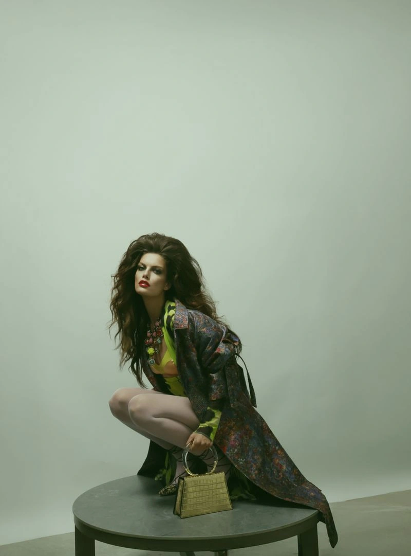 Model Vanessa Fuchs crouching on a pedestal in a patterned coat and holding a handbag for Numero Switzerland