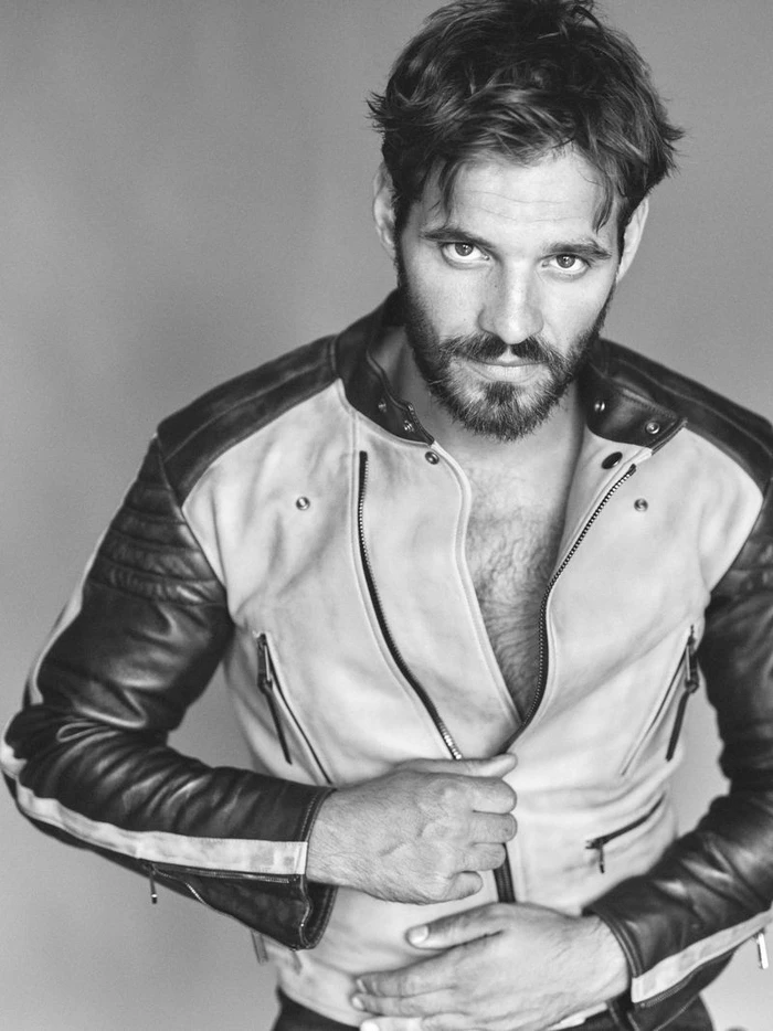 Man wearing a contrasting panel leather jacket pulling the zipper against a plain grey backdrop