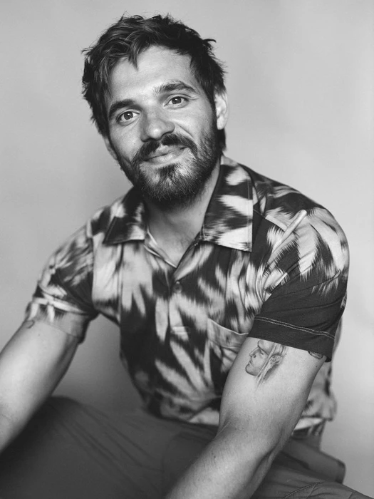 Portrait of Tyler Conti wearing a patterned short-sleeve shirt against a seamless background in monochrome.