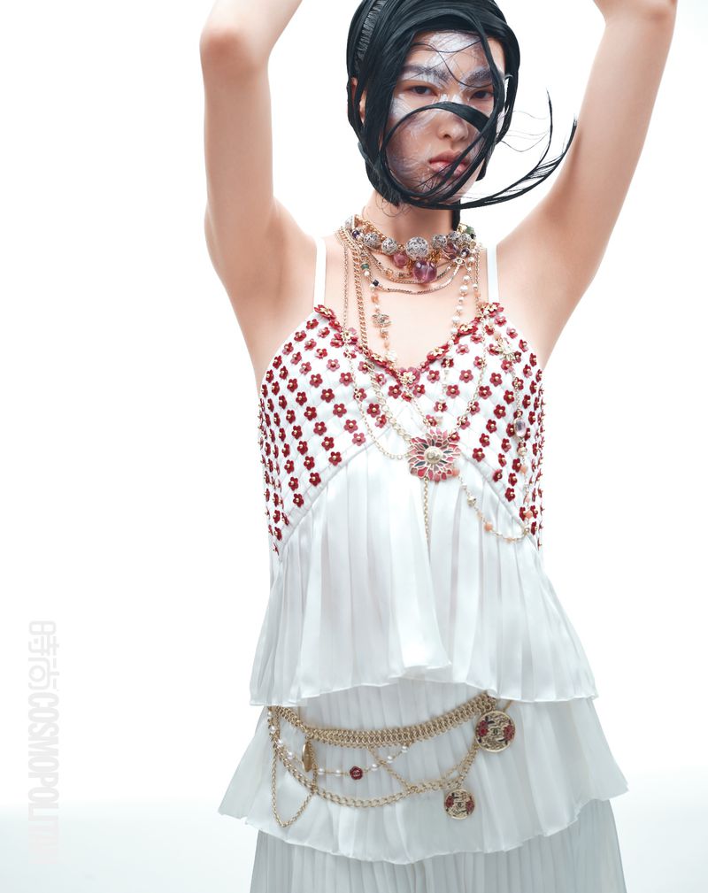 Asian woman in editorial fashion shot with white ruffled tiered top and layered necklace against a white background in studio lighting.