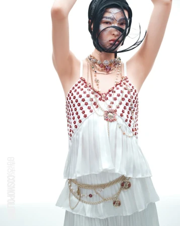 Asian woman in editorial fashion shot with white ruffled tiered top and layered necklace against a white background in studio lighting.