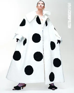 Model in a voluminous white coat with large black polka dots against a plain studio background for Cosmopolitan China