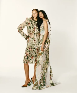 Two female models posing together in floral embroidered dresses against a plain white studio background.