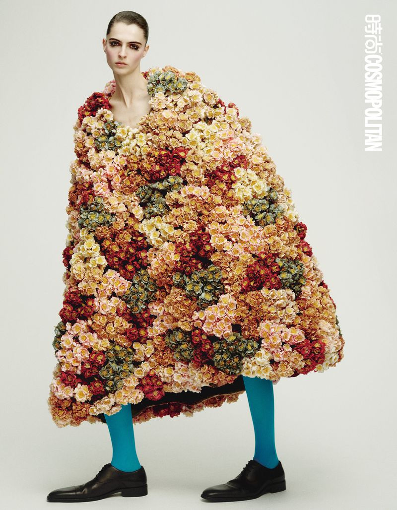 Model wearing a voluminous floral cape and bright blue tights against a plain white studio background.