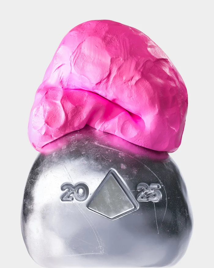 Pink clay mass resting on top of a metallic silver object with embossed numbers and a triangular cutout against a white background.