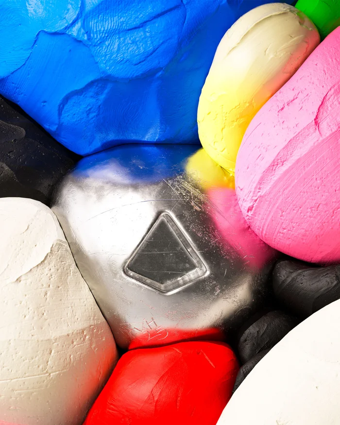 Close-up abstract view of colourful sculpted shapes featuring a central metallic silver form with a triangular indentation next to red, blue, yellow, and pink blocks.