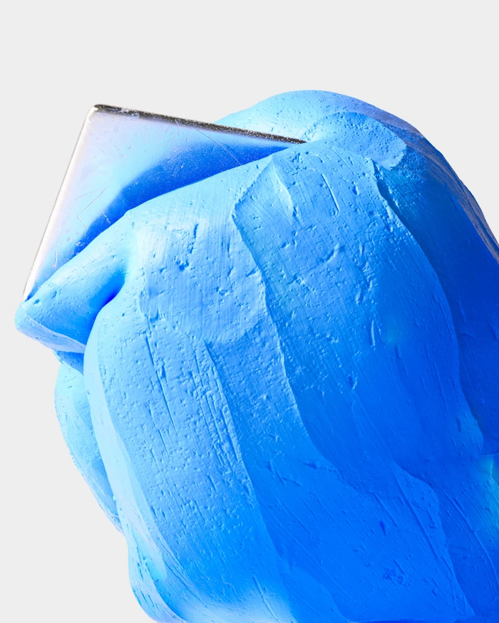 Textured blue sculptural head object with a metallic rectangular plate emerging from the top against a white background
