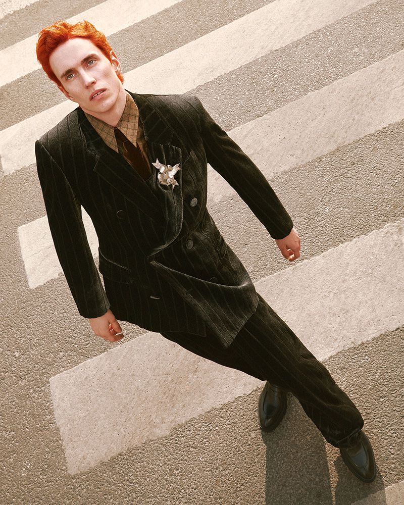 Man in a pinstripe suit stands on a crosswalk, looking up. The shot uses a high angle, capturing the man's formal attire and the urban setting.