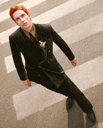 Red-haired male model wearing a dark double-breasted pinstripe suit walking across a pedestrian crosswalk