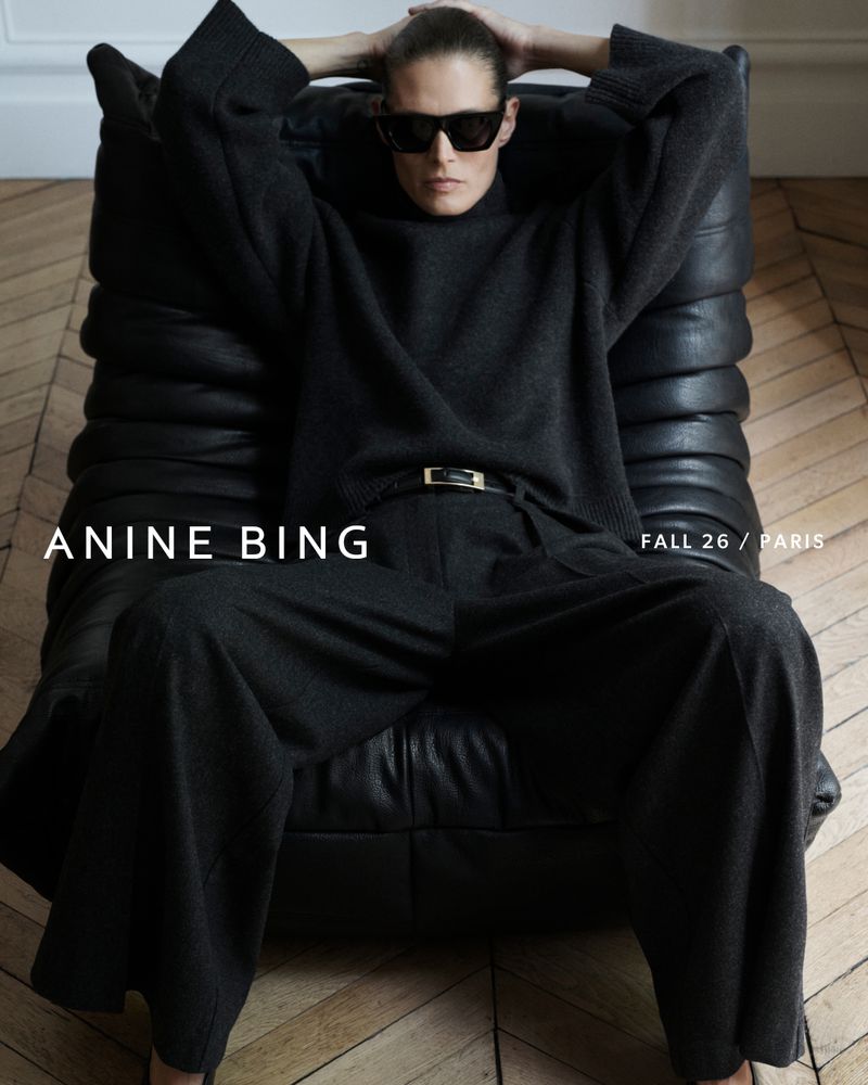 Model Malgosia Bela seated in a black leather armchair wearing a dark sweater and sunglasses for Anine Bing Fall 2026