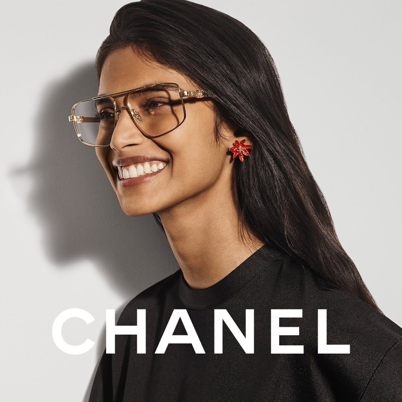 Model wearing gold-framed glasses and red flower earrings against a plain white background with Chanel branding