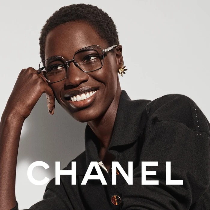 Model wearing eyeglasses and black top with gold buttons in front of a white background with Chanel typography