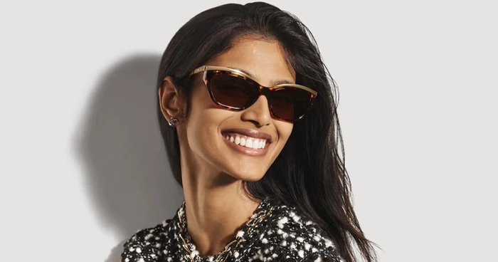 Model wearing tortoiseshell sunglasses and a black and white tweed top against a plain light background