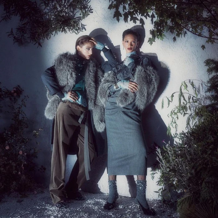 Two models wearing textured winter fashion against a textured wall with shadows and foliage overhead.
