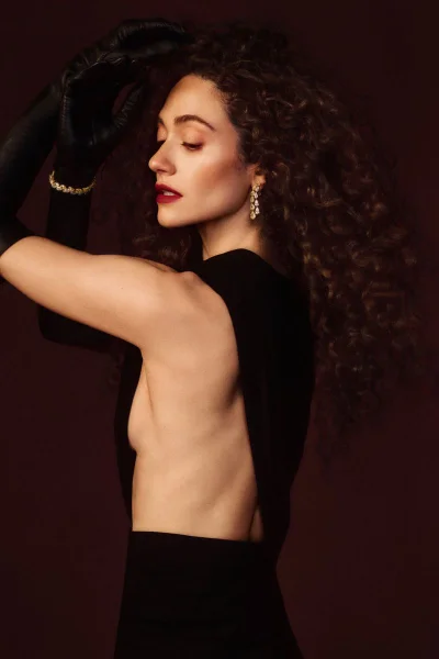 Emmy Rossum wearing a black dress and opera gloves with long curly hair in an editorial portrait for InStyle U.S.