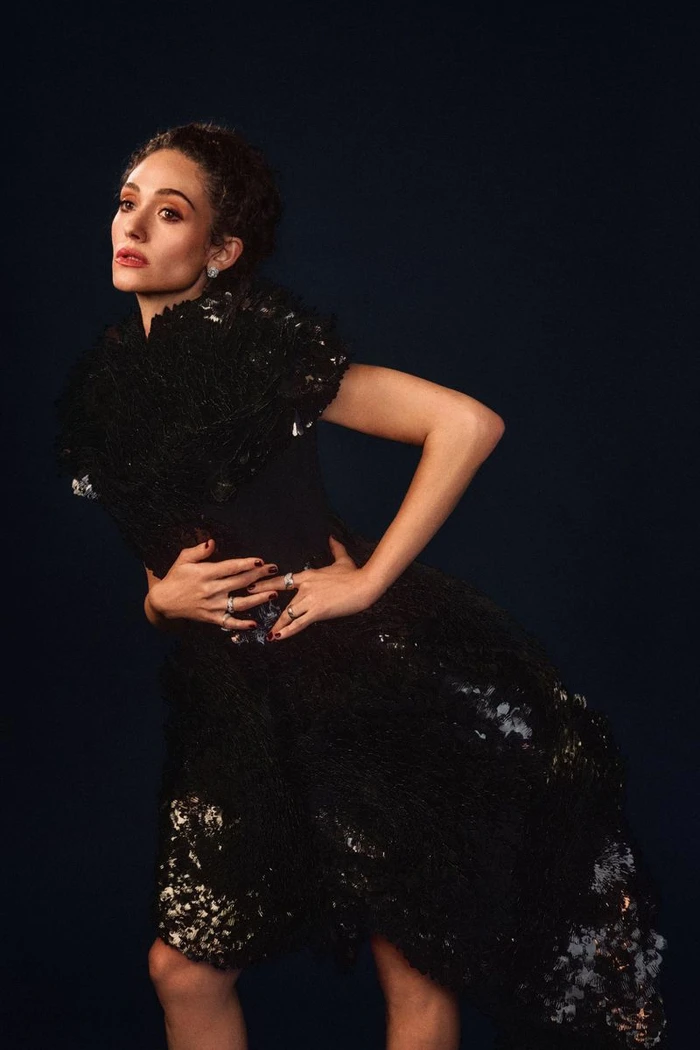 Emmy Rossum posing in a sculptural black textured dress against a dark background for InStyle U.S.