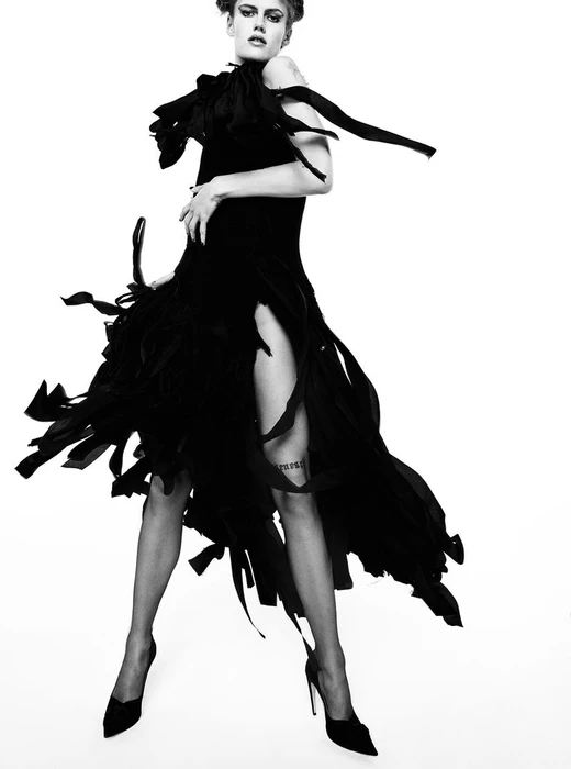 Model Lucia Richardson wearing a black fringed dress and heels against a white seamless background for Beyond Noise.