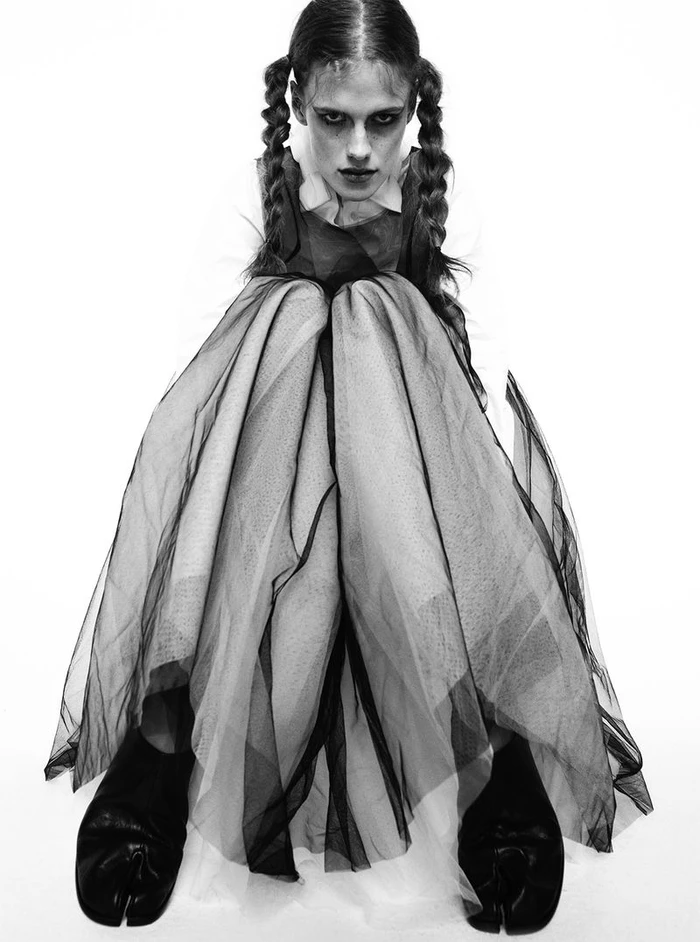Model Lucia Richard with braided pigtails wearing a sheer layered skirt against a white background