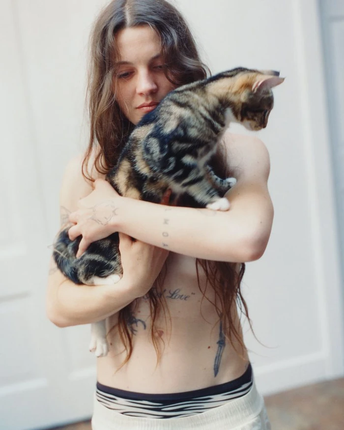 Woman holding a tabby kitten against a plain light background for More or Less Magazine editorial