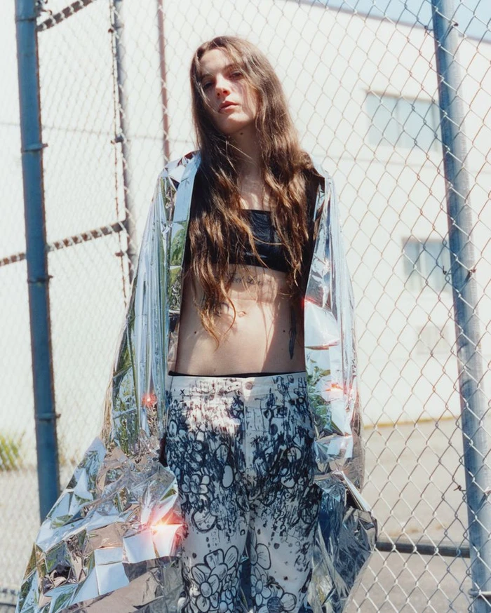 Woman wrapped in a shiny metallic emergency blanket standing in front of chain-link fence