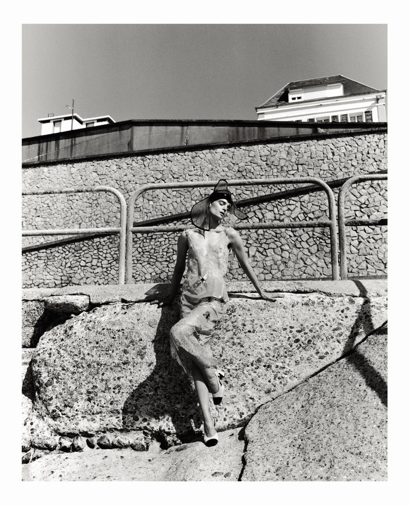 Model in sheer dress and statement hat leaning against stone wall outdoors by Tarek Mawad for Mode Metieres