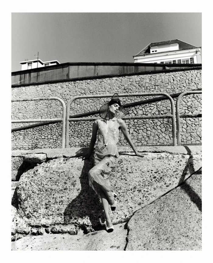 Model in sheer dress and statement hat leaning against stone wall outdoors by Tarek Mawad for Mode Metieres