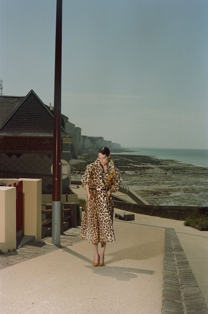 Model in a leopard print coat standing on a coastal pathway near cliffs and water for a Les Echos fashion editorial.