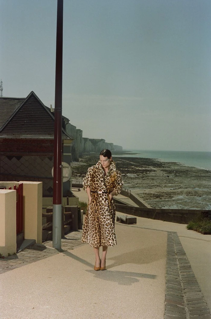Model in a leopard print coat standing on a coastal pathway near cliffs and water for a Les Echos fashion editorial.