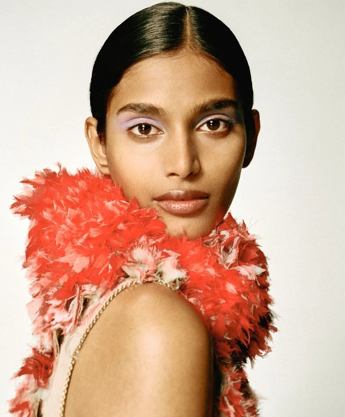 Close-up portrait of a model wearing a vibrant red feathered garment against a plain light background