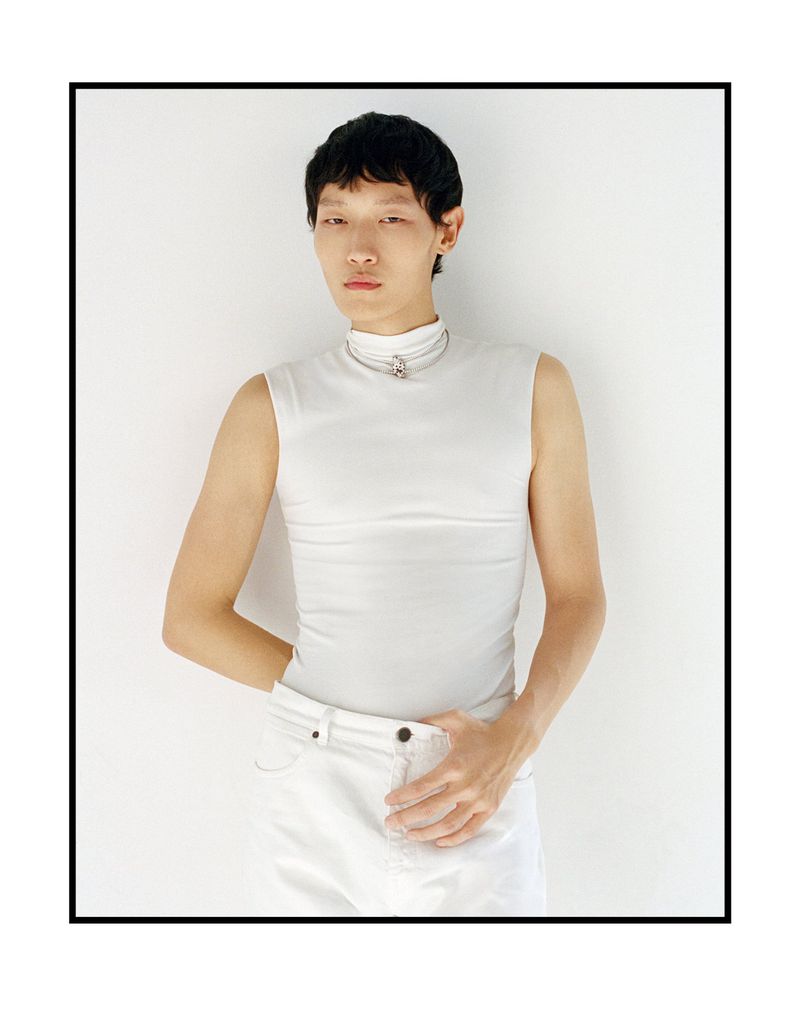 Asian male model wearing a white sleeveless turtleneck top and white trousers against a light background