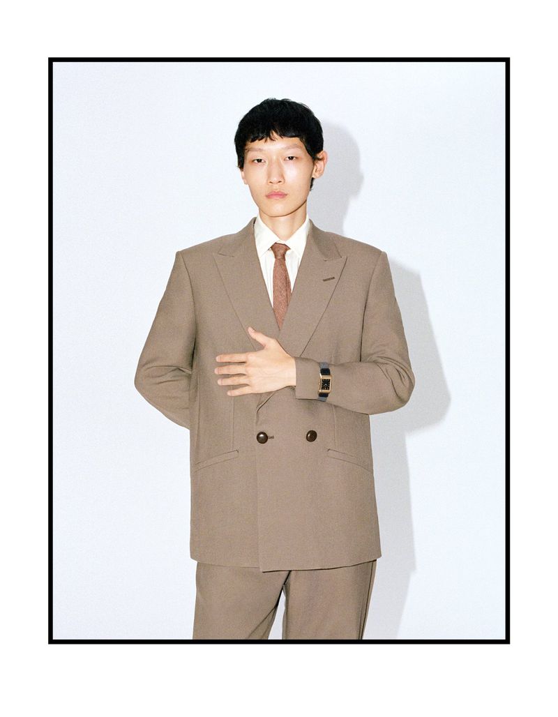 Model wearing a double-breasted brown suit and tie against a plain white studio background.