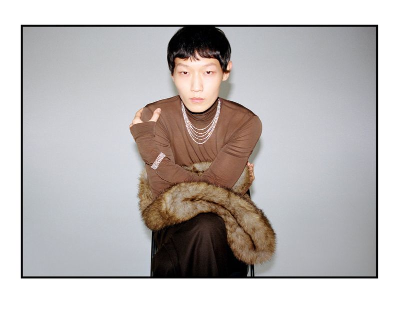 Asian man wearing a brown turtleneck and layered necklaces with a fur wrap for Esquire China