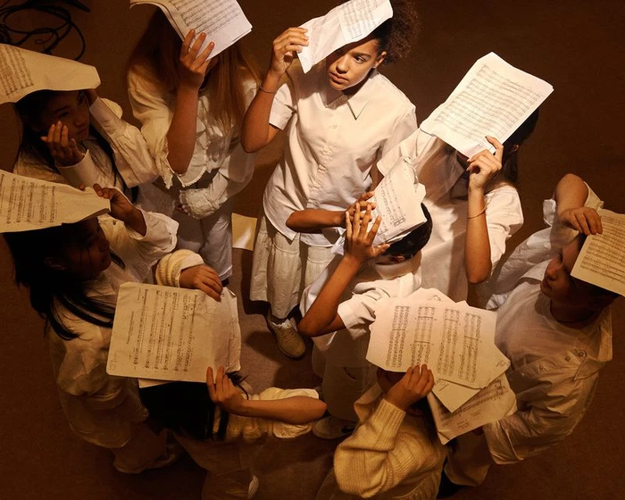 Group of children wearing white shirts holding sheets of music over their heads in a circle for Vogue Italia