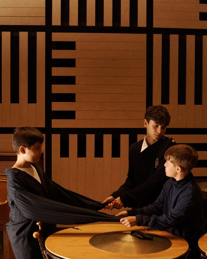 Three young boys interacting around a round wooden table against a geometric patterned wood wall for Vogue Italia.