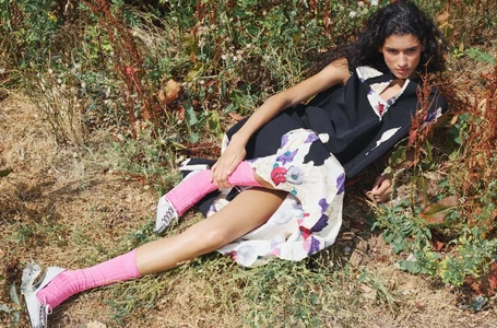 Model lying in a grassy meadow wearing a dark dress with a floral skirt and bright pink socks
