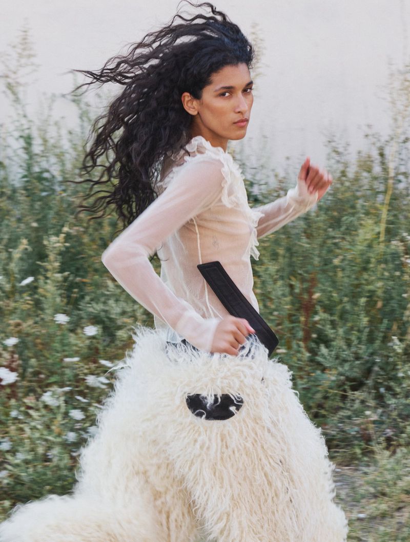 Model with long dark hair running outdoors wearing a sheer white ruffled top and a voluminous textured white skirt