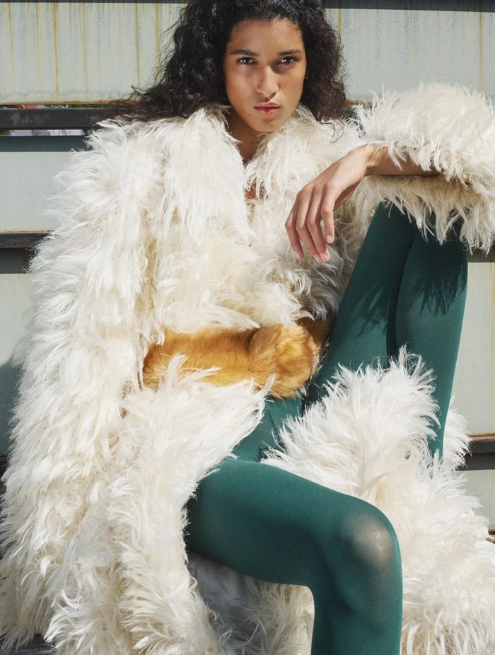 Model with dark curly hair wearing a fluffy white faux fur coat and green leggings for CR Fashion Book.